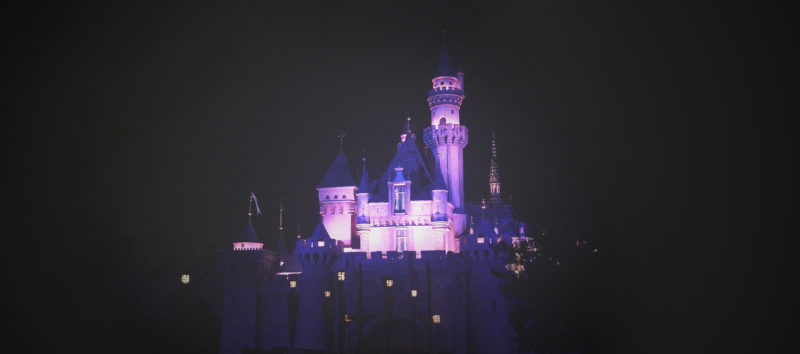 The Disney castle lit up in pink at night.